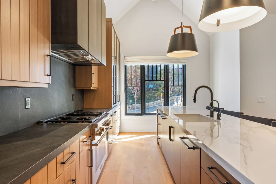 Sleek kitchen design with black countertops, white cabinetry, and large windows letting in natural light.
