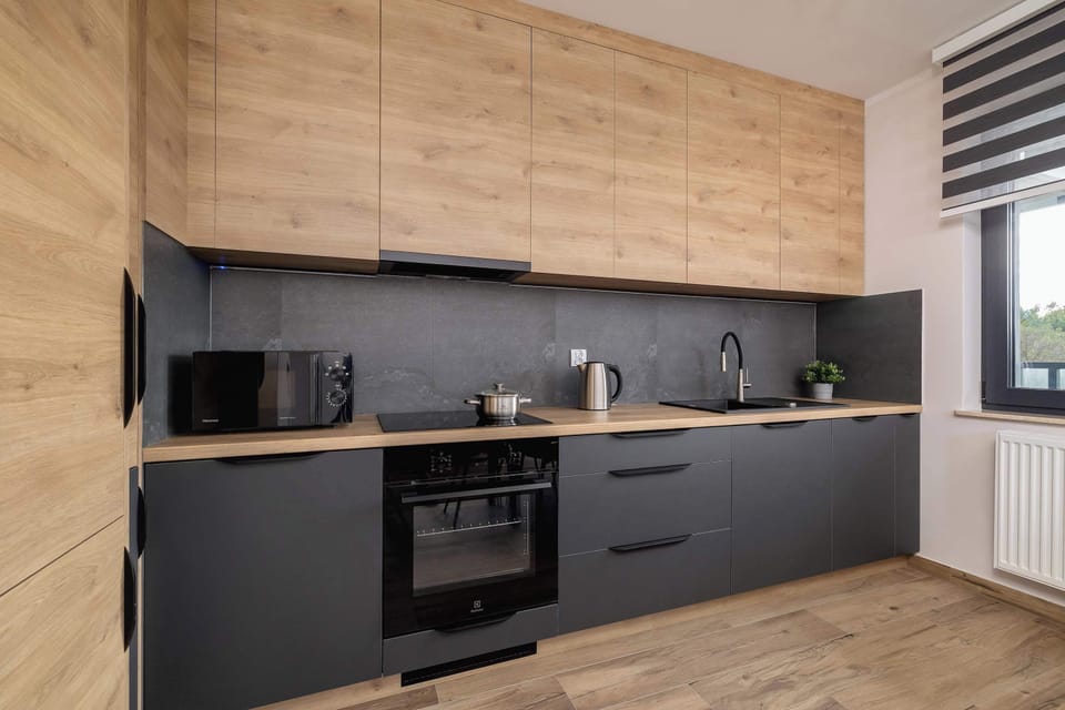 A sleek kitchen area with dark cabinetry, modern appliances, and a wooden counter, next to what appears to be a living space.