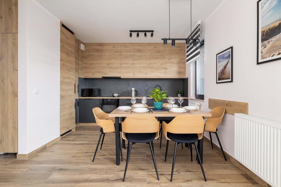 A modern kitchen and dining area with dark lower cabinets, light upper cabinets, and a wooden dining table with chairs.