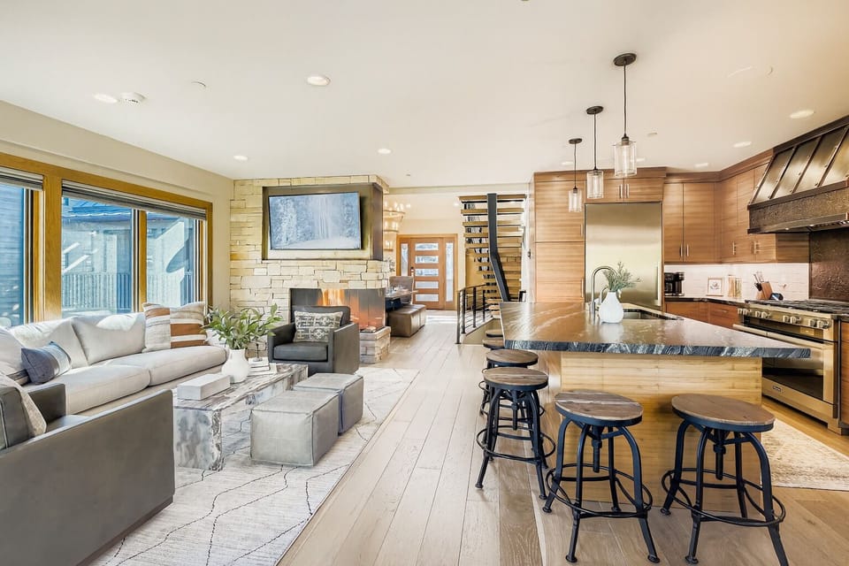 Relax in this chic open-concept living area featuring a cozy fireplace, large TV, full kitchen with bar seating, and stylish decor. Perfect for entertaining or unwinding after a day of adventure.