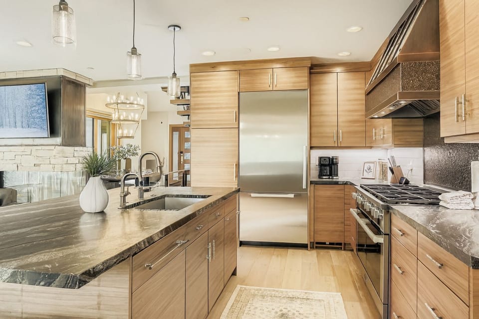 Prepare meals in our fully equipped kitchen, featuring a large island with a sink, modern stainless steel appliances, and a stylish wood-paneled design. All the essentials for a great stay.