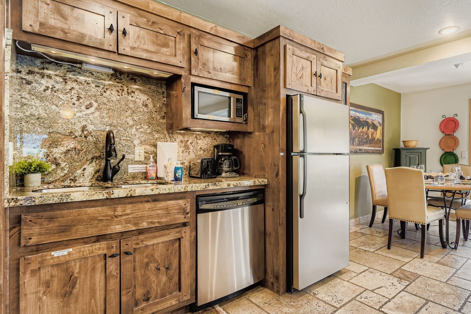 A fully equipped kitchenette with rustic wood cabinetry, granite countertops, and stainless steel appliances.