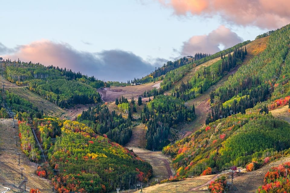 Mountain valley showcases brilliant autumn foliage with vibrant reds, oranges, and yellows painting the hillsides beneath dramatic evening sky.