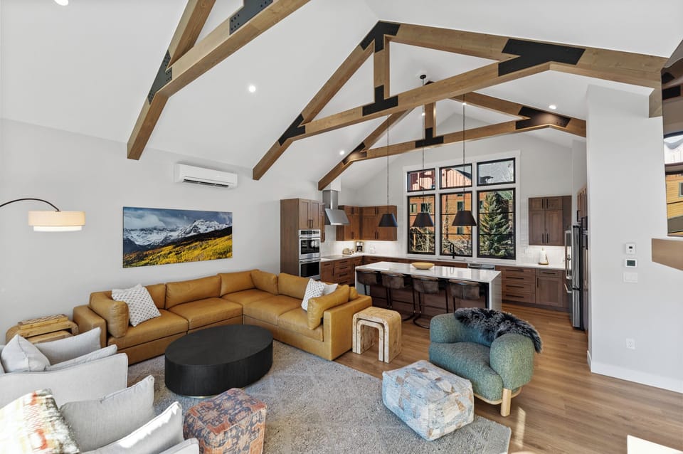 Relax in your open-concept living space with soaring wood beams, modern kitchen, and mountain artwork creating the perfect alpine retreat atmosphere.