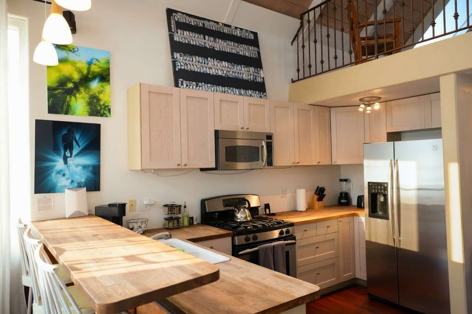 A beautiful kitchen with stainless steel appliances, and a stylish breakfast bar. The airy layout features high ceilings and a view of the charming mezzanine loft.