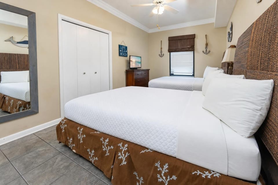 A cozy guest bedroom features two full beds, white linens, a dresser, and beach-themed decor, creating a relaxed atmosphere