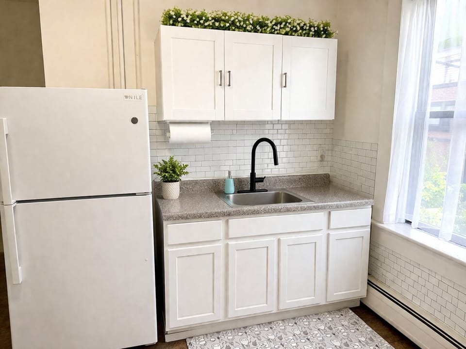 Bright, modern kitchenette with full fridge, subway tile, sunny window.