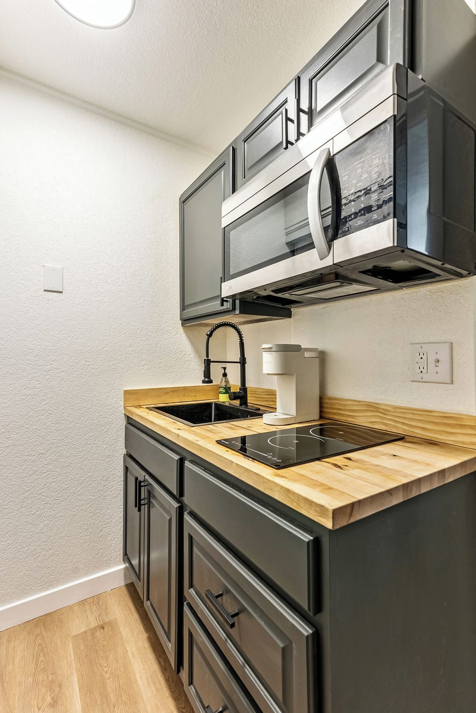 A sleek kitchenette featuring, a black sink, microwave, a dual-burner stove  and a keurig machine- ideal for simple, efficient meal prep.