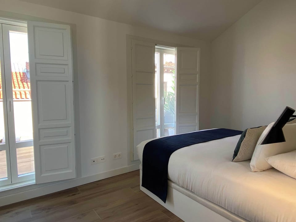 A bedroom with a bed and light coming through shuttered windows.