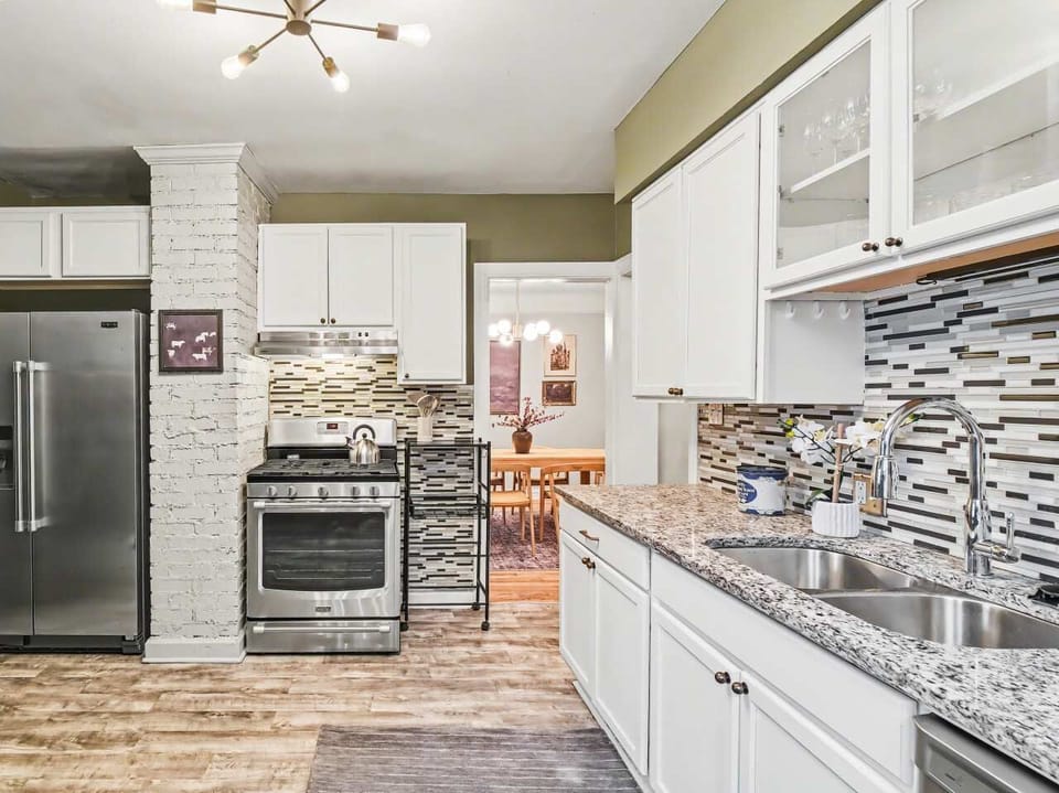 Prepare meals in this bright, open kitchen featuring premium granite countertops, crisp white cabinetry, and high-end stainless steel appliances. The warm wood floors and sleek tile backsplash create a perfect, welcoming space.