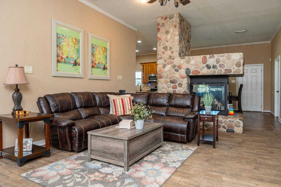 Warm living room with plush seating, rustic stone fireplace, hardwood floors, free Wi-Fi, and central AC & heat