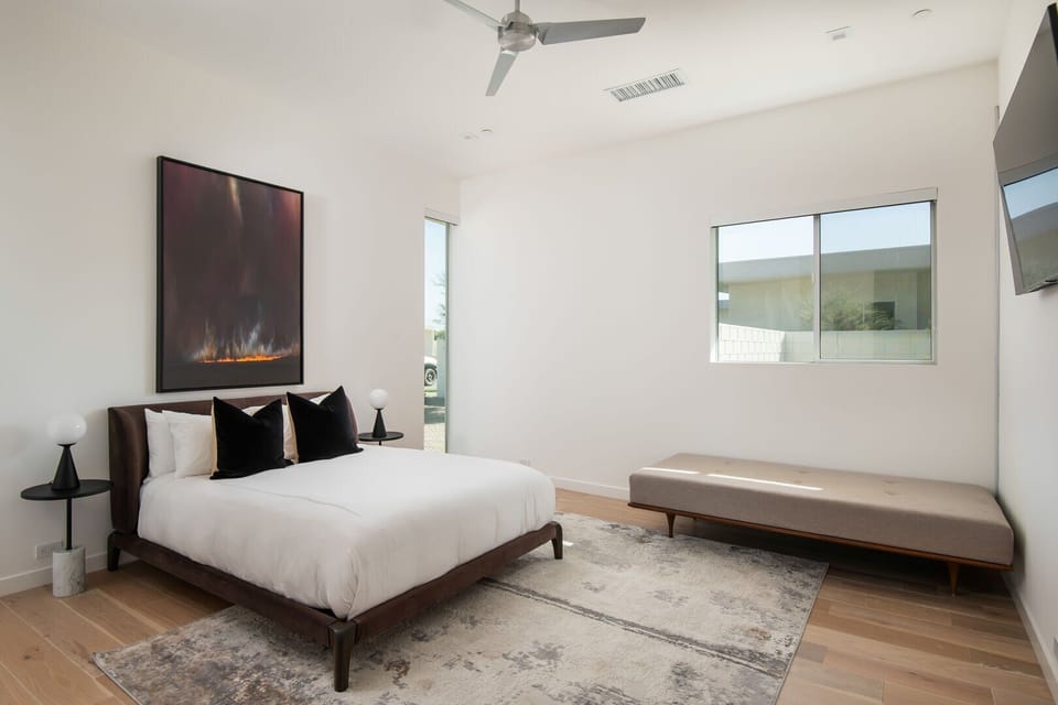 A bright and tranquil queen bedroom, featuring modern art, plush bedding, and an elegant chaise lounge.