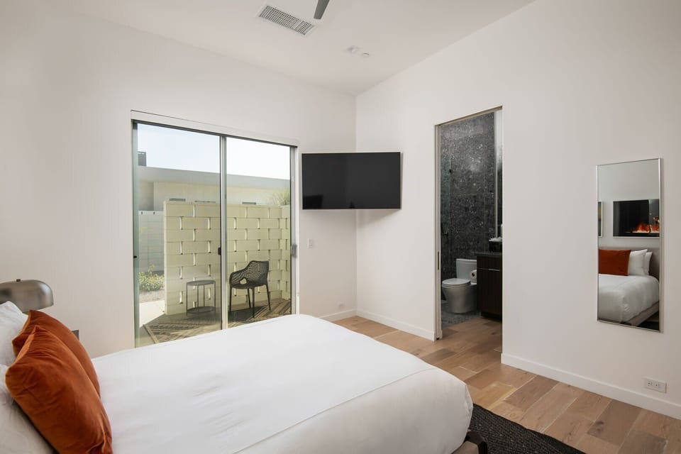 A serene queen suite with a wall-mounted smart TV and an ensuite bathroom, offering private access to the outdoor spaces.