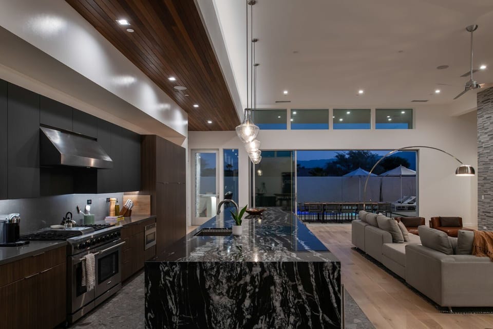 Experience true indoor-outdoor living at twilight, with the living area, gourmet kitchen, and bar seamlessly flowing to the illuminated pool deck.