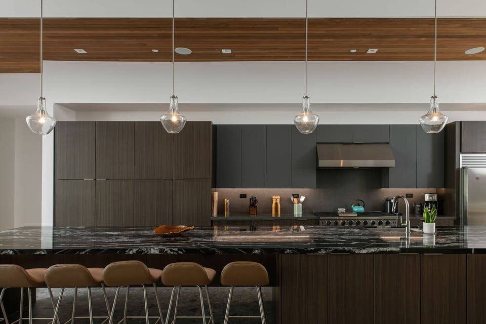 A close-up view of the gourmet kitchen island, highlighting the striking black marble, bar seating, and stylish pendant lighting.