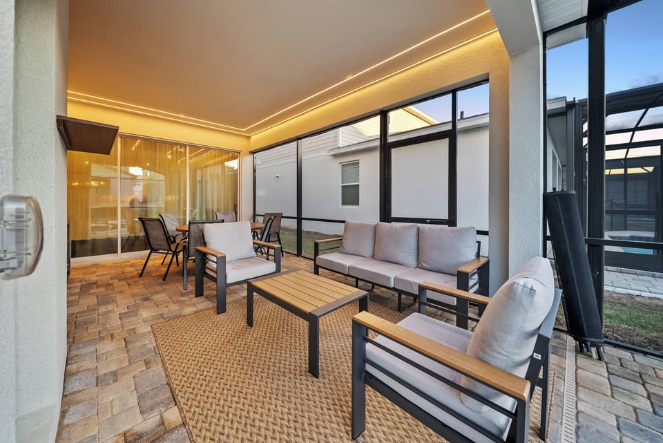 Relax in a charming screened porch with cozy seating and plush cushions, where soft evening light creates a warm atmosphere. Large windows bring the outdoors in, providing the perfect setting to unwind and enjoy your time.
