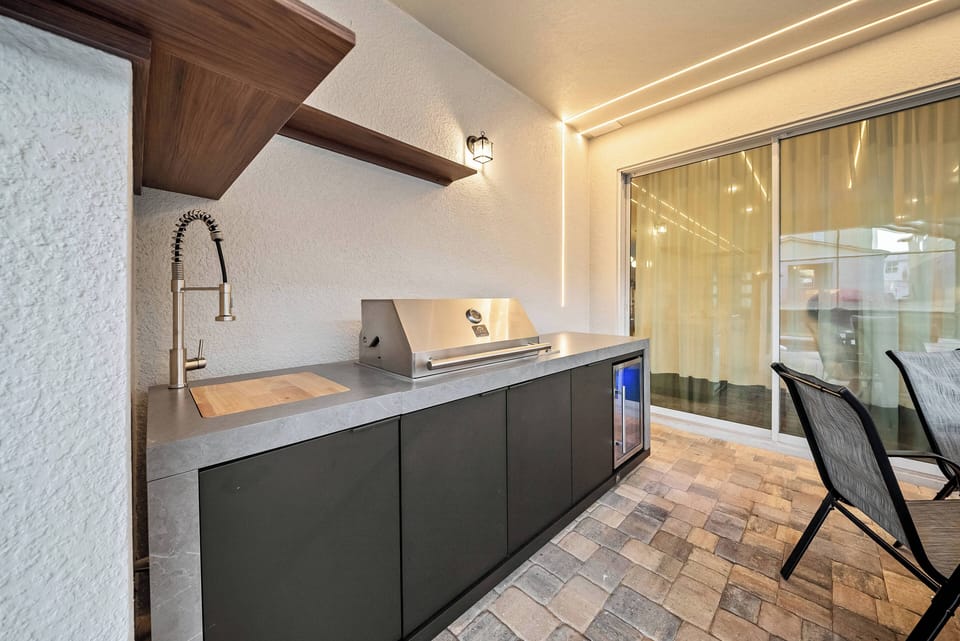 Discover a culinary haven with sleek charcoal cabinetry and a spacious concrete countertop, perfect for meal prep. Natural light pours in through large sliding doors, accentuating the warm wood details and inviting atmosphere.