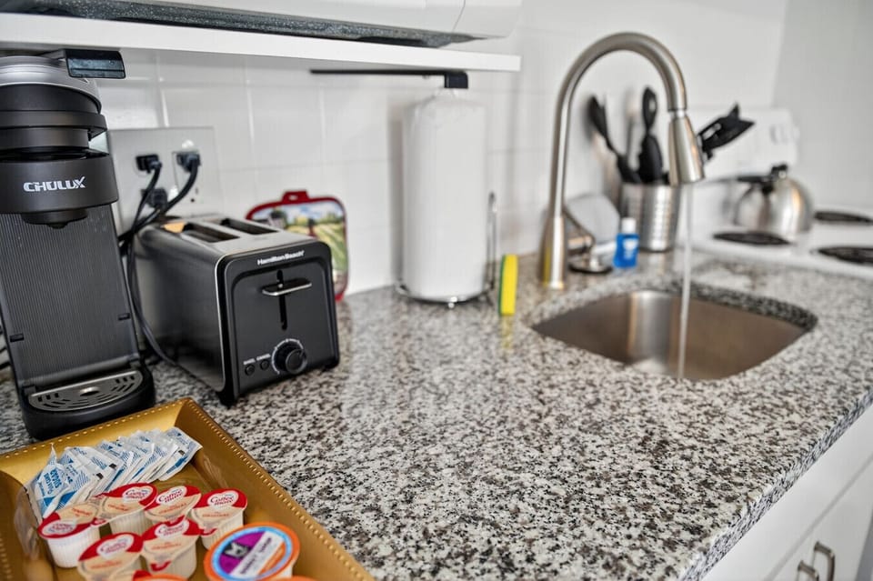 Close-up of the kitchen sink area w/ granite counters & essentials ready for daily use.
