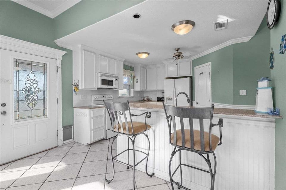 Kitchen with breakfast bar seating, white cabinets, refrigerator, microwave, and bright coastal interior finishes.