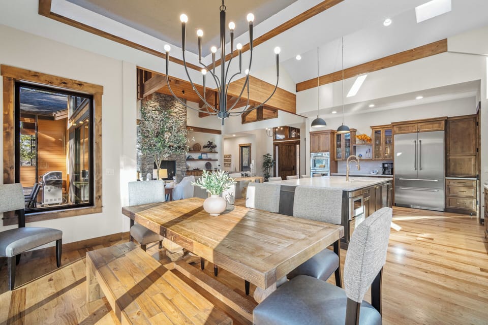 Gather around your rustic dining table beneath soaring ceilings, where warm wood and modern elegance create the perfect backdrop for memorable meals.