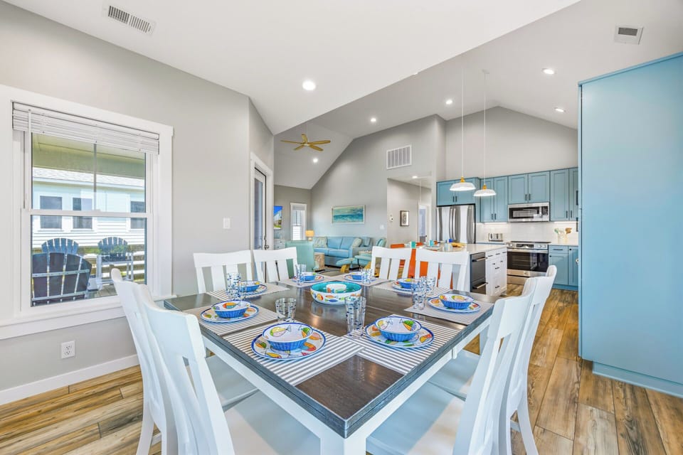 Gather around this cheerful dining table with seating for eight, perfectly positioned to enjoy the bright, open-concept living and kitchen area. Cheerful coastal-inspired tableware and soaring vaulted ceilings create a welcoming atmosphere for your group m