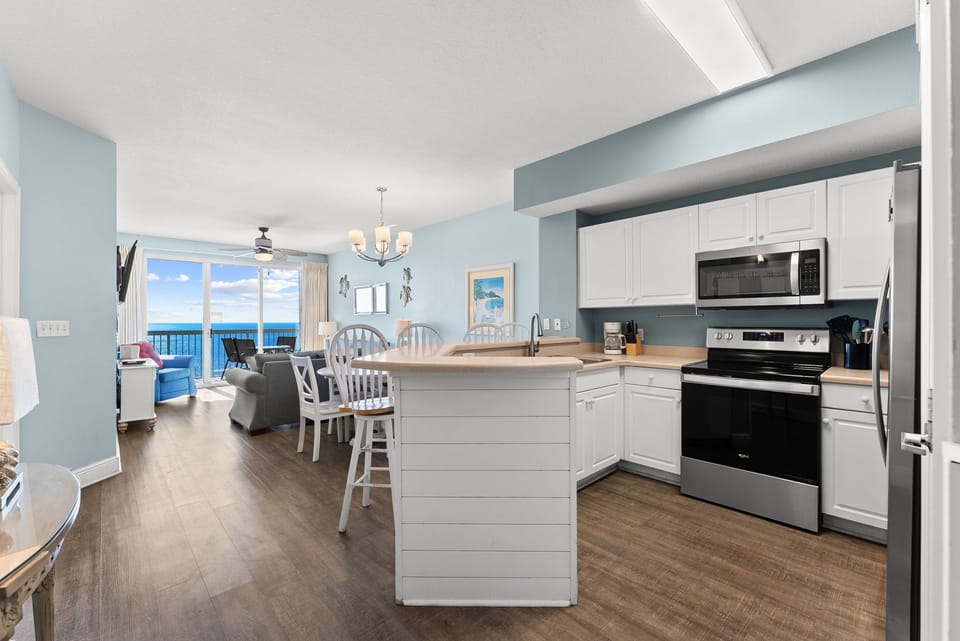 Bright, open kitchen w/ island seating, modern appliances, & ocean views from the dining area.