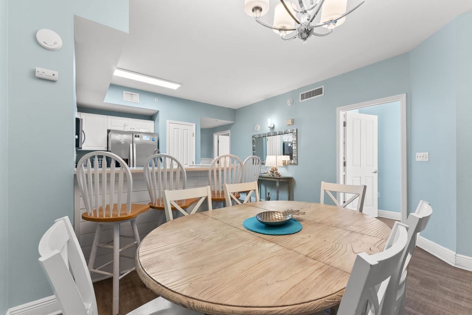 Airy dining nook w/ a round wood table, chandelier, & soft coastal blue walls.