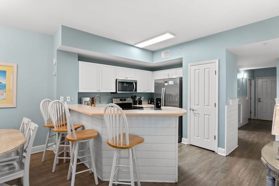 Clean white kitchen w/ bar seating, stainless steel appliances, & plenty of counter space.