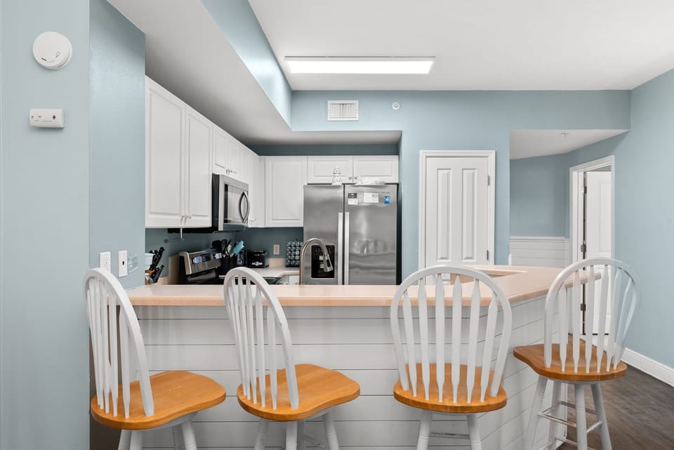 Functional kitchen w/ bar stools, stainless steel appliances, & a bright, open layout.