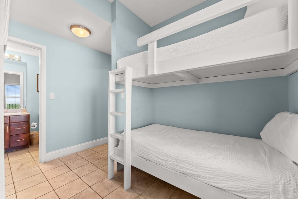 Compact bedroom featuring a white bunk bed with light blue walls and tiled flooring.