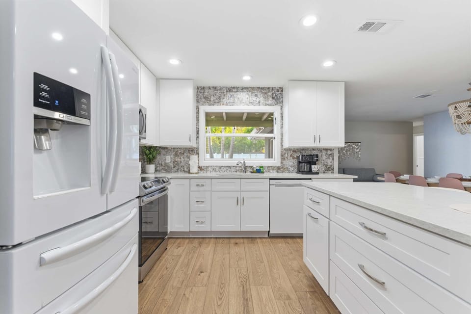 Spacious, sunlit kitchen with sleek white cabinetry, stainless appliances, and a large island for cooking or gathering. The perfect blend of modern design and comfort—ideal for sharing meals and making memories.