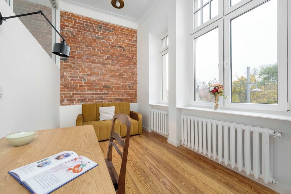 A bright corner with a brick accent wall and large window. A cozy reading chair sits beside the radiator.