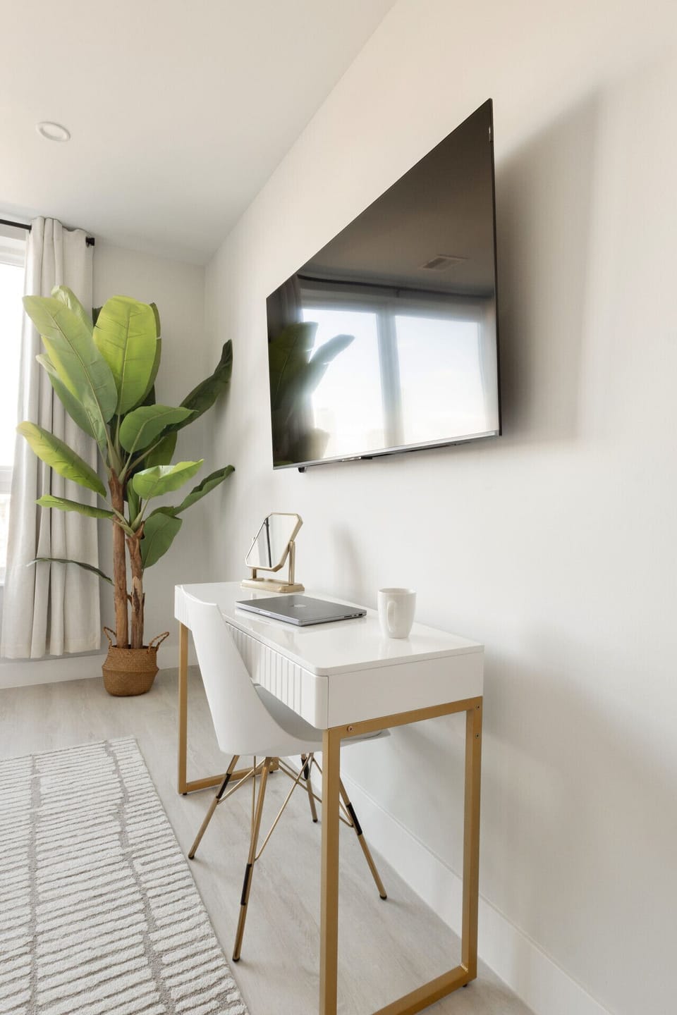 Desk, vanity mirror, plant, desk chair, plant, 55` TV