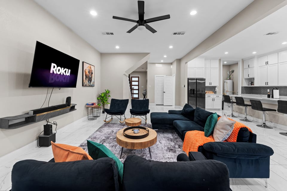 Cozy living room with navy seats, bright pillows, wood tables, and Roku TV.