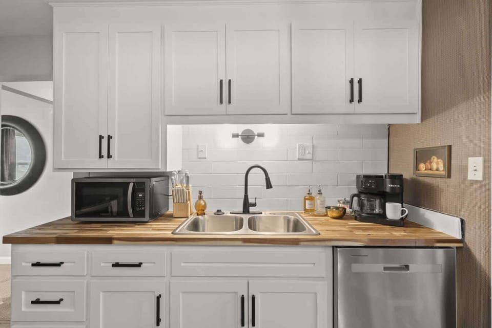 Another kitchen angle showing generous counters, farmhouse sink & bright finishes.