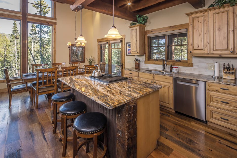 This stunning kitchen showcases rustic wood cabinetry, a striking island, and expansive windows that frame beautiful forest views. | Main Level