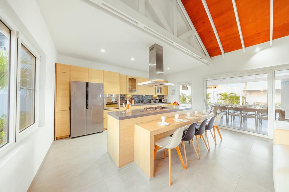 Modern open kitchen with large island, full-size fridge, and outdoor dining view.
