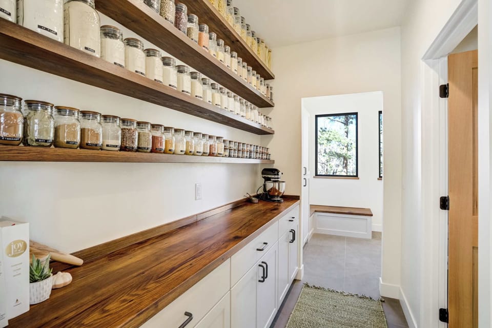This beautifully organized pantry showcases custom shelving, warm wood counters, and thoughtful design that complements the kitchen’s refined craftsmanship.