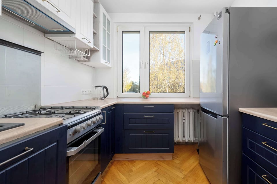 A compact kitchen with blue cabinets, wooden floors, and a small window. The design is practical and aesthetically pleasing.