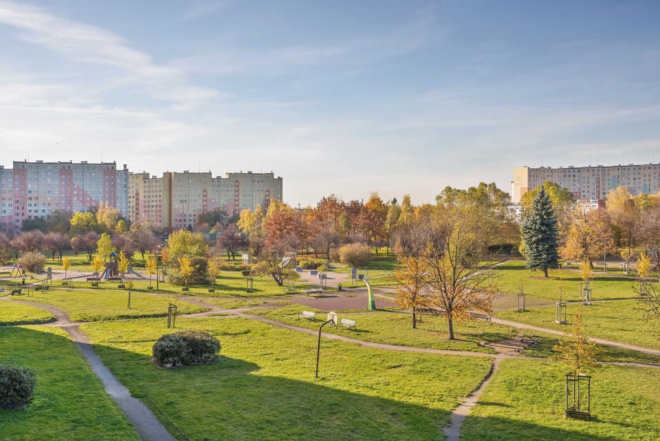 A view of the surrounding residential area with green grass, trees, and apartment buildings. The sky is clear and the weather appears sunny.