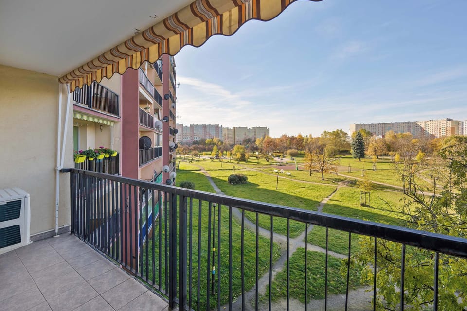 A balcony view overlooking grassy courtyards and nearby buildings. The space provides an open and airy perspective.