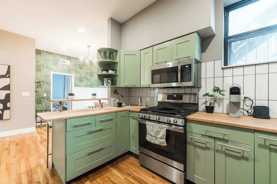 Modern kitchen with sage green cabinets, stainless steel appliances, and wood countertops. Bright and functional layout with a large window, perfect for cooking and enjoying a cozy, stylish space.
