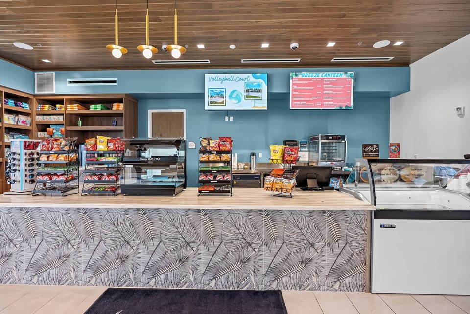 Welcome to a vibrant space with a sleek marble countertop, warm wooden ceiling, and soft blue walls. Enjoy our well-organized shelves stocked with snacks and drinks, inviting you to relax and indulge at your leisure.
