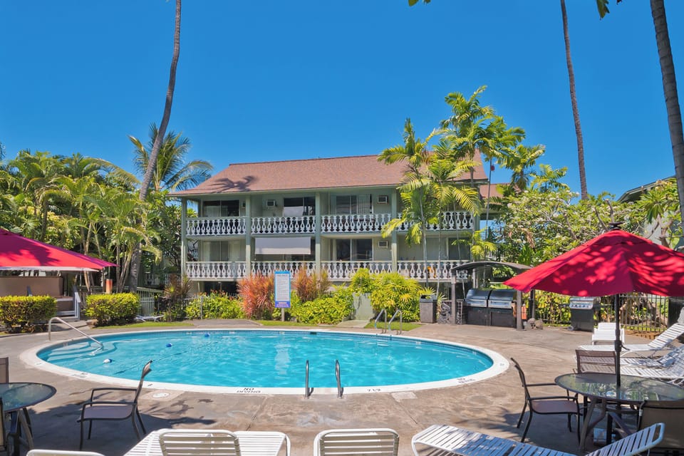 A sparkling pool sits beneath swaying palms, framed by the property's charming balconies and lush tropical gardens—your perfect spot to soak up sunny Hawaiian days.