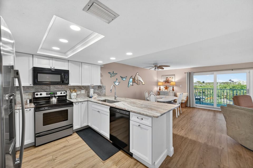 Bright, open kitchen w/ white cabinetry, stone counters & a seamless flow into the dining & living area