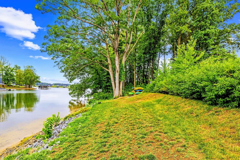 Waterfront - A gentle lawn meets the rip-rap shoreline, with kayaks staged under shade trees and calm cove water beyond.