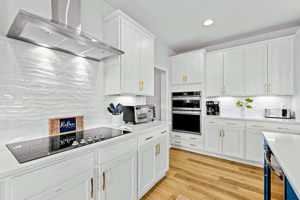 Kitchen - White shaker cabinetry, a five-burner cooktop under a stainless hood, and double wall ovens make group dinners easy.