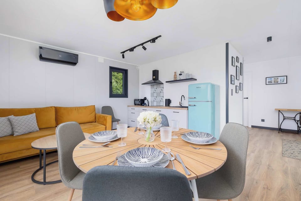 A cozy living space combining a sitting area and dining table beside large windows. The yellow furniture and soft lighting create a warm mood.