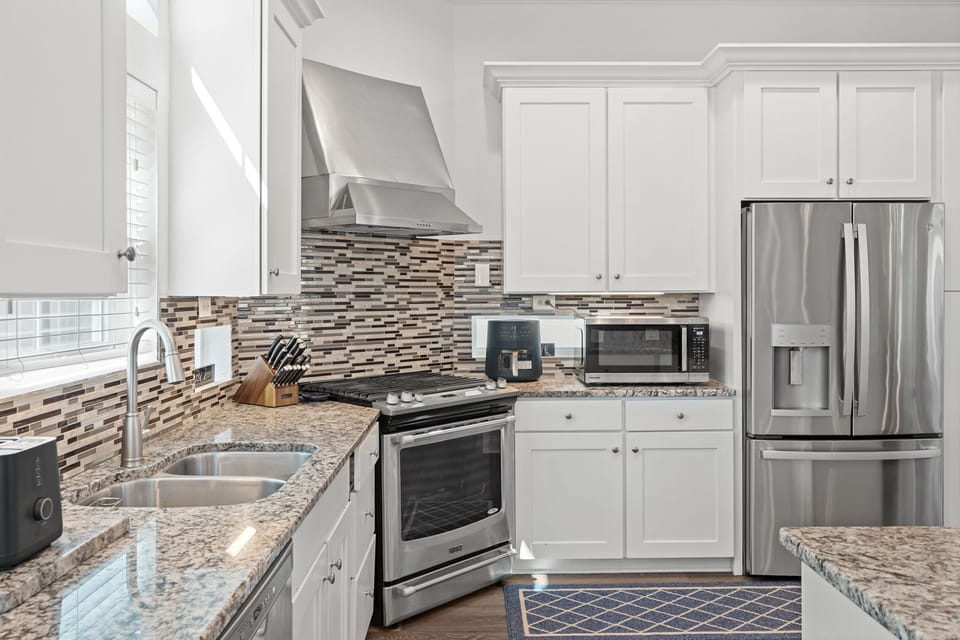 Modern coastal kitchen with sleek stainless steel appliances, granite countertops, and a mosaic backsplash—blending style and function for effortless seaside living.