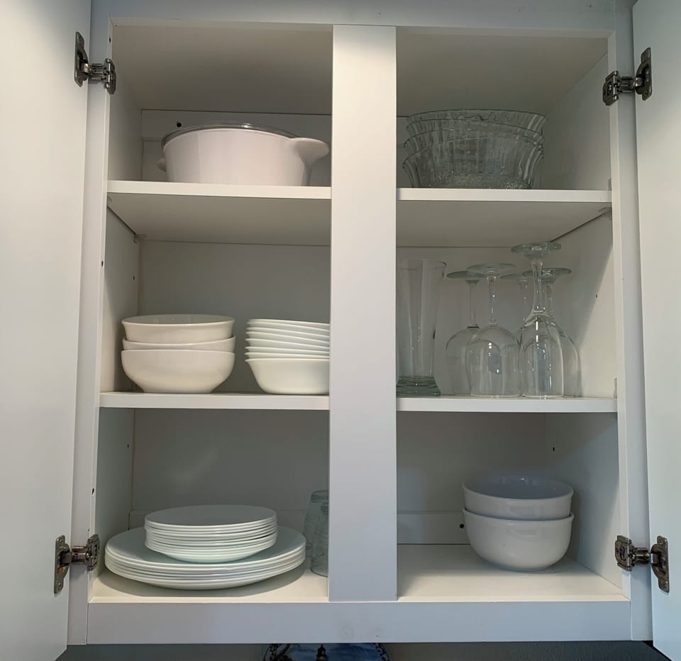 White plates, bowls, and glassware displayed cleanly in cabinet.